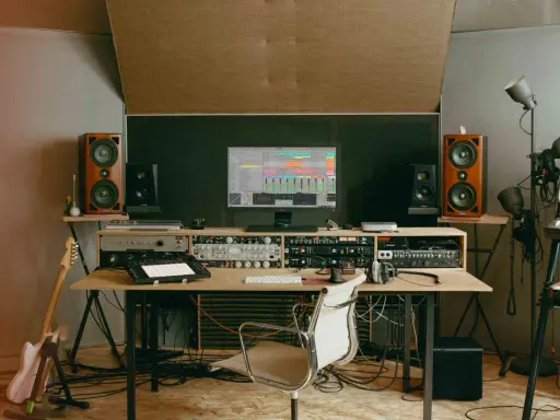 Un studio d'enregistrement avec des enceintes, un ordinateur affichant une station de travail audio numérique, des claviers, une guitare et divers équipements. C'est ici que le producteur de musique crée des sons.