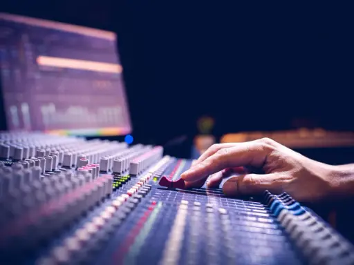Main d'un ingénieur du son ajustant les curseurs d'une console de mixage pour optimiser la phase audio.
