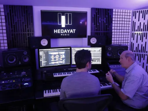 Deux hommes travaillent dans un studio d'enregistrement, le logo HEDAYAT MUSIC est visible sur un écran.