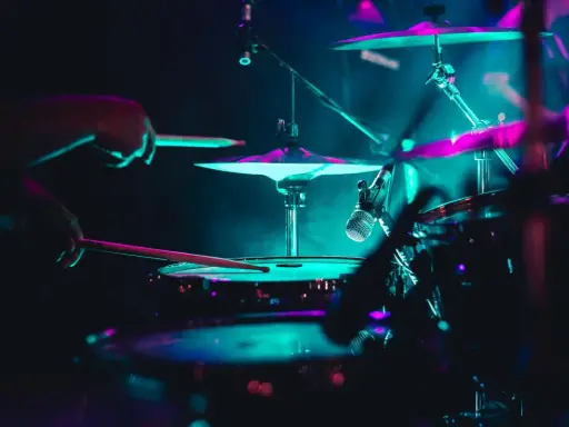 Mains d'un batteur frappant la caisse claire, avec des cymbales illuminées de néons. La **musique accompagnement batterie** crée une ambiance électrique.