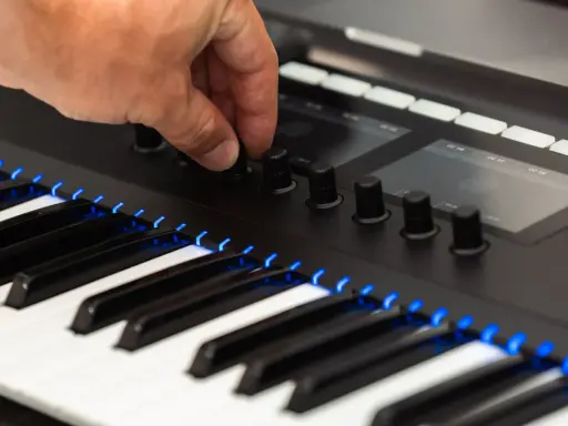 Main d'un musicien ajustant un bouton sur un clavier de musique numérique, avec des touches illuminées de bleu.