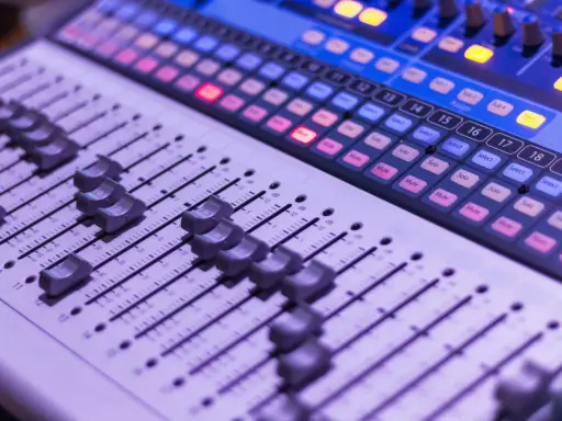Console de mixage avec des curseurs et des boutons lumineux, prête pour une session d'enregistrement.