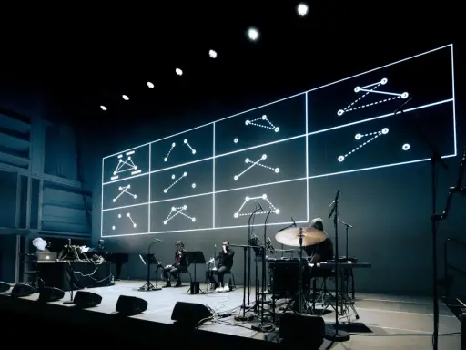 Sur scène, des musiciens jouent devant un écran projetant des schémas lumineux. Une performance pour comment se faire remarquer.