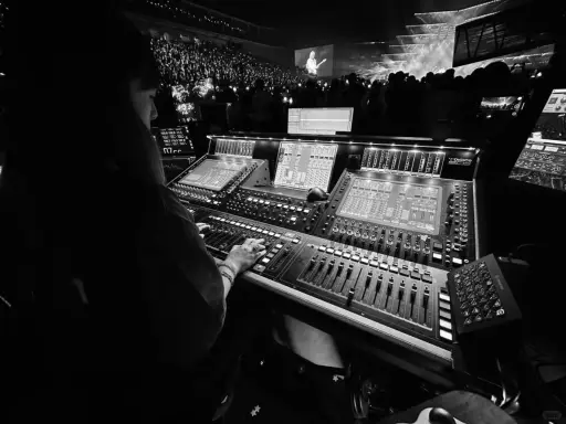 Une personne manipule une console de mixage dans un studio d'enregistrement, devant une foule lors d'un concert.