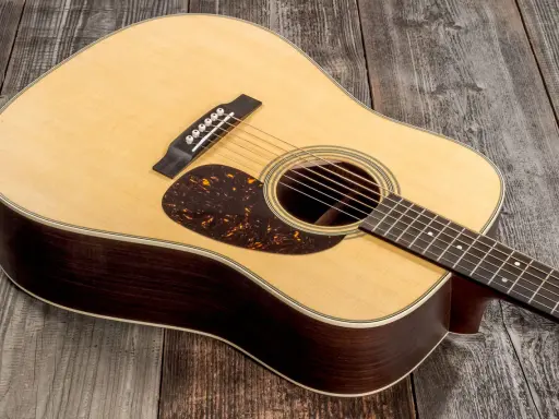 Une guitare acoustique Martin D-28, avec son corps en bois sombre et sa table claire, repose sur un fond de planches de bois grises.