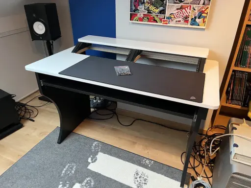 Bureau d'angle noir et blanc, prêt pour faire de la musique sur PC. Haut-parleur, tapis de souris et étagères pour équipement audio.