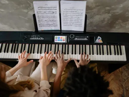 Deux mains jouent un accord c/b piano, des partitions sur le pupitre.