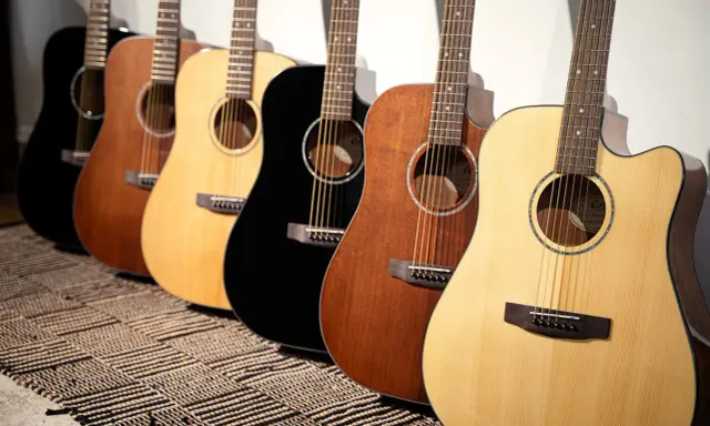 Une rangée de guitares acoustiques Cort, noires, marron et naturelles, posées sur un tapis rayé.