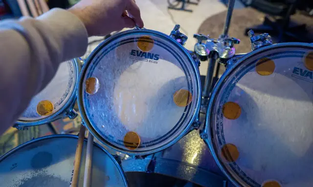 Main d'un batteur ajustant un timbre sur une peau de batterie Evans, prêt à monter une batterie pour un concert.