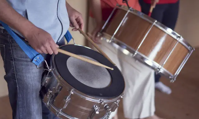 Des musiciens jouent de la percussion brésilienne, leurs mains tenant des baguettes prêtes à frapper les tambours.