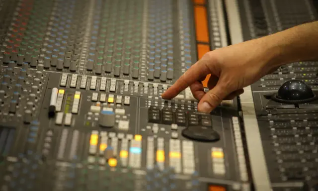 Main d'un ingénieur du son ajustant les faders d'une console de mixage, créant un son audio mono parfait.