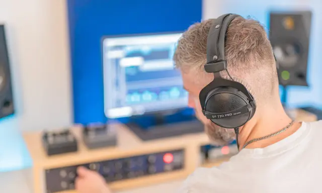 Un homme avec un casque sur les oreilles ajuste les réglages sur une console pour faire un EP dans son studio d'enregistrement.