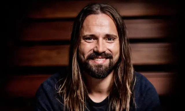Un homme souriant aux longs cheveux bruns et à la barbe, peut-être un des compagnons d'écriture de Max Martin.