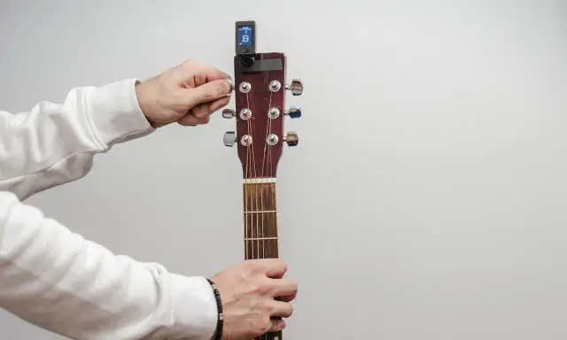 Main tenant de la guitare, il utilise un accordeur pour accorder l'instrument.