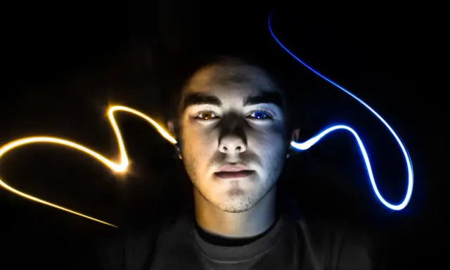 Visage d'un jeune homme éclairé par des traînées de lumière jaune et bleue, évoquant un ia mixage audio créatif.