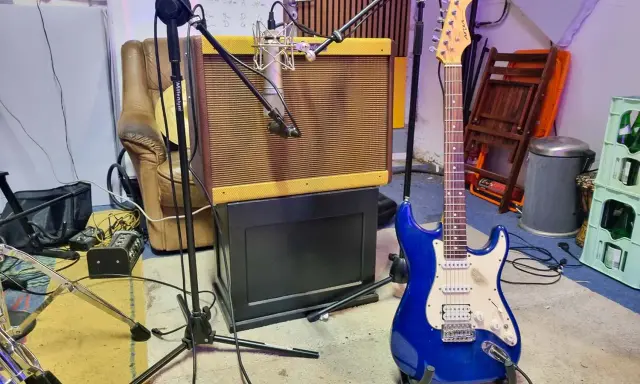 Une guitare électrique bleue étincelante est prête à jouer dans un studio d'enregistrement, à côté d'un ampli vintage et d'un fauteuil usé.