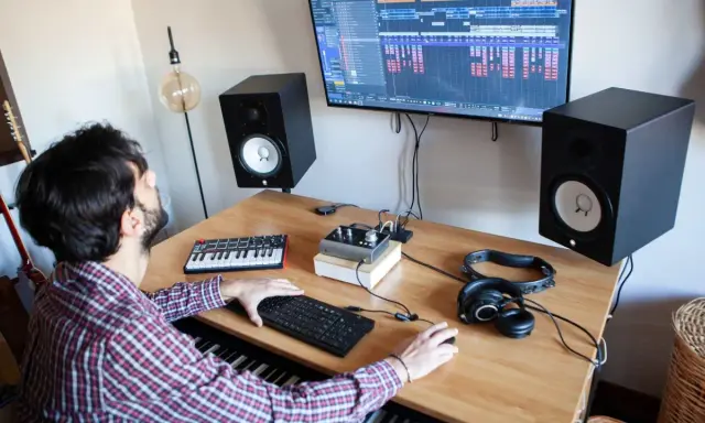 Un homme crée de la musique dans son studio. Il utilise un clavier, un ordinateur et des enceintes pour apprendre comment écrire un son.
