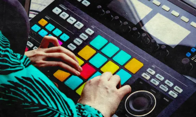 Mains d'un musicien jouant sur un instrument midi coloré, créant des rythmes avec les pads lumineux.