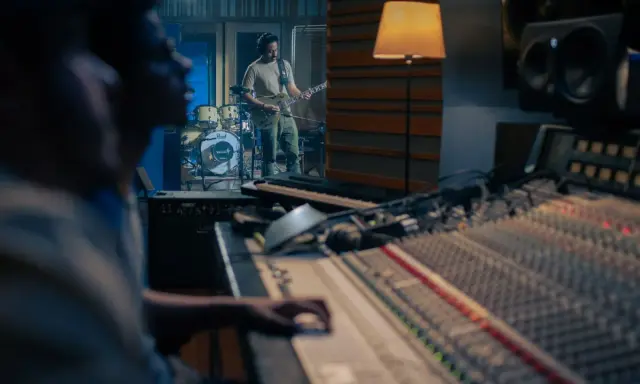 Un guitariste joue dans un studio d'enregistrement, tandis qu'un ingénieur du son est prêt à comment mixer la musique sur la console.