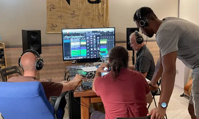 Trois hommes en formation mastering dans un studio d'enregistrement, concentrés sur un écran affichant une console de mixage numérique.