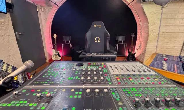 Console de mixage analogique dans un studio d'enregistrement, avec guitares et fauteuil de gamer.