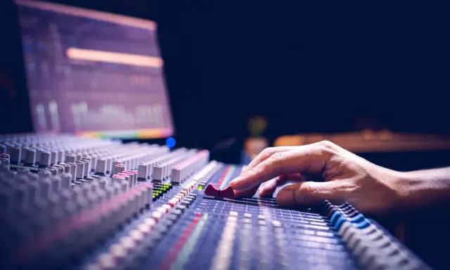 Main d'un ingénieur du son ajustant les curseurs d'une console de mixage pour optimiser la phase audio.