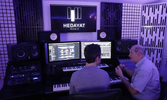 Deux hommes travaillent dans un studio d'enregistrement, le logo HEDAYAT MUSIC est visible sur un écran.