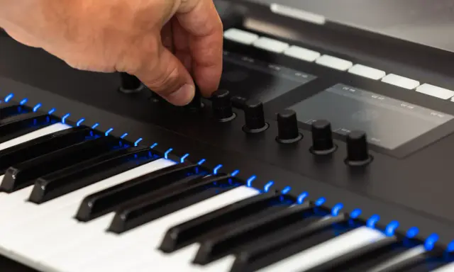 Main d'un musicien ajustant un bouton sur un clavier de musique numérique, avec des touches illuminées de bleu.