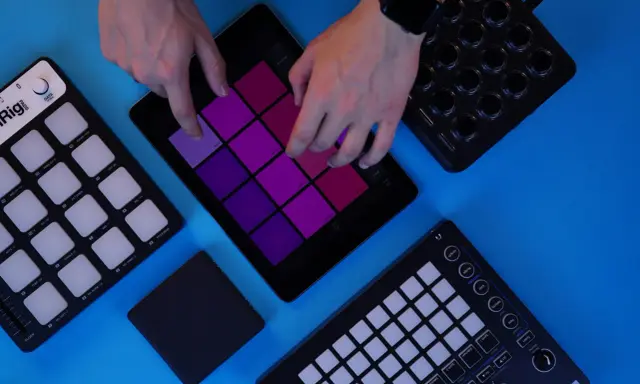 Des mains jouent sur une tablette avec des pads colorés, entourée de contrôleurs pour créer de la musique. Un sampler sans ordinateur en action.