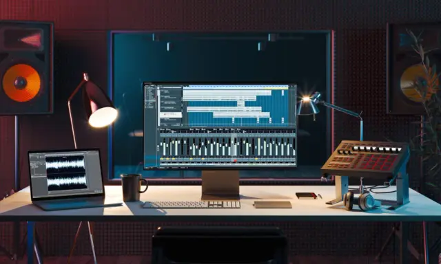 Studio d'enregistrement avec ordinateur affichant une station de travail audio numérique, un clavier, des enceintes et un pad de batterie, le tout constituant du matériel pour composer musique électronique.