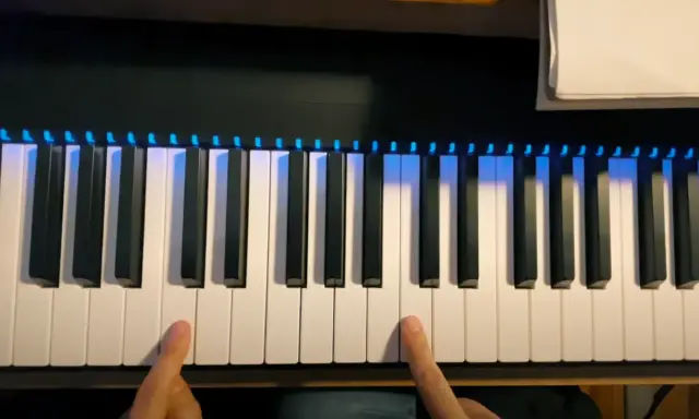 Deux doigts prêts à jouer un accord sur un piano numérique avec des lumières bleues illuminant les touches.