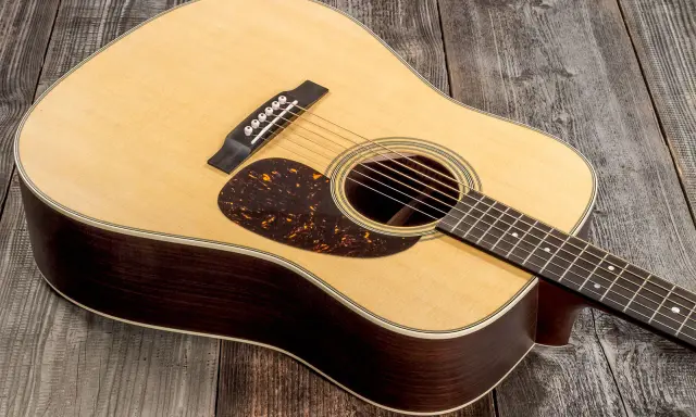 Une guitare acoustique Martin D-28, avec son corps en bois sombre et sa table claire, repose sur un fond de planches de bois grises.
