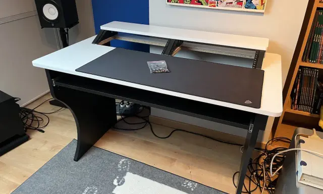 Bureau d'angle noir et blanc, prêt pour faire de la musique sur PC. Haut-parleur, tapis de souris et étagères pour équipement audio.