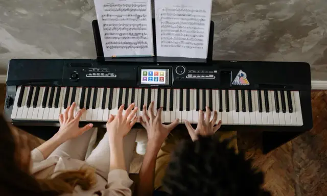 Deux mains jouent un accord c/b piano, des partitions sur le pupitre.