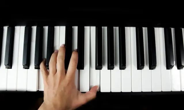 Main gauche jouant le sol 7 piano, doigts effleurant les touches noires et blanches.
