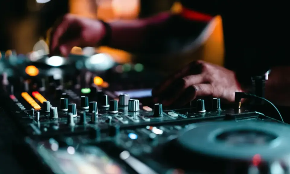 Mains d'un DJ en pleine action, manipulant les boutons pour apprendre à mixer. Lumières colorées et ambiance nocturne.
