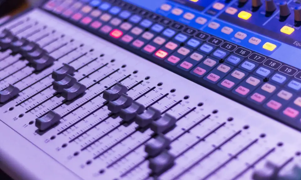 Console de mixage avec des curseurs et des boutons lumineux, prête pour une session d'enregistrement.