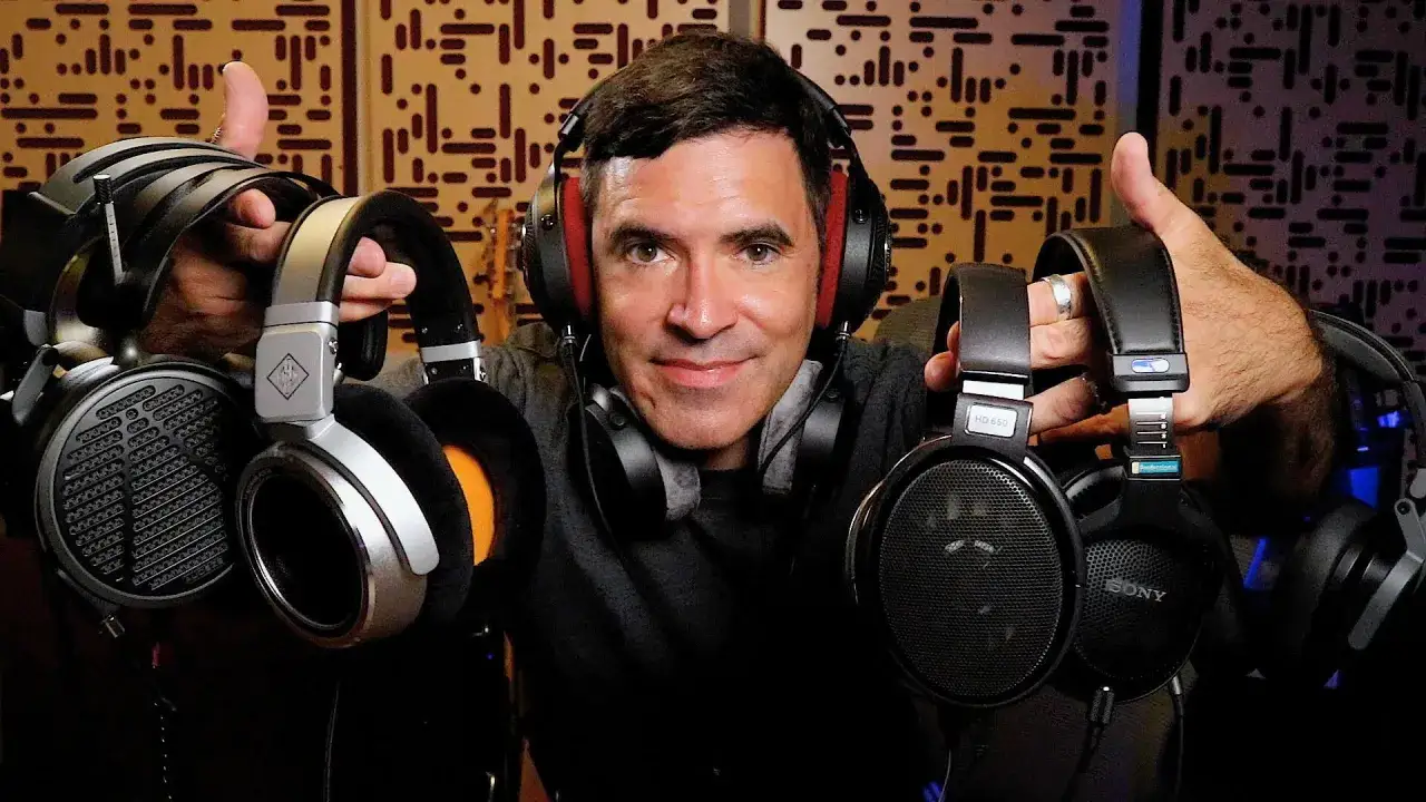Un homme souriant, portant un casque audio, présente plusieurs autres casques. Il est dans un studio d'enregistrement, prêt pour un mixer au casque.