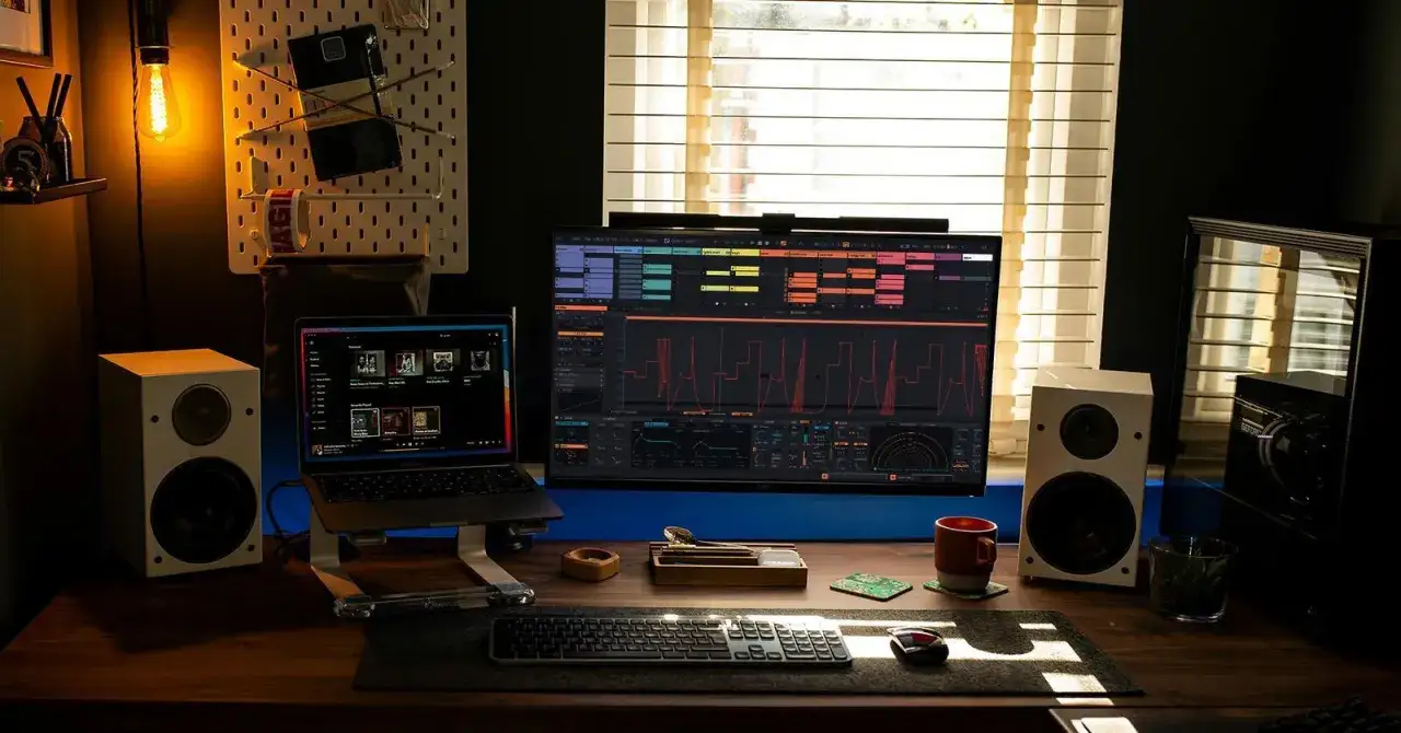 Bureau avec ordinateur affichant un logiciel de musique, deux enceintes, un clavier et une tasse. L'utilisateur utilise daw linux pour cr&eacute;er de la musique.
