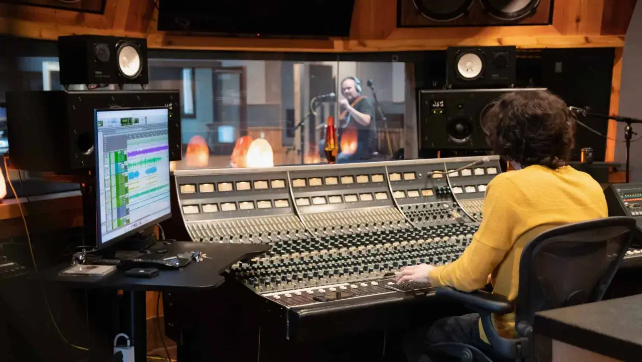 Ingénieur du son ajustant les réglages sur une console, cherchant le son parfait avec un effet de plate reverb pour le chanteur dans le studio.