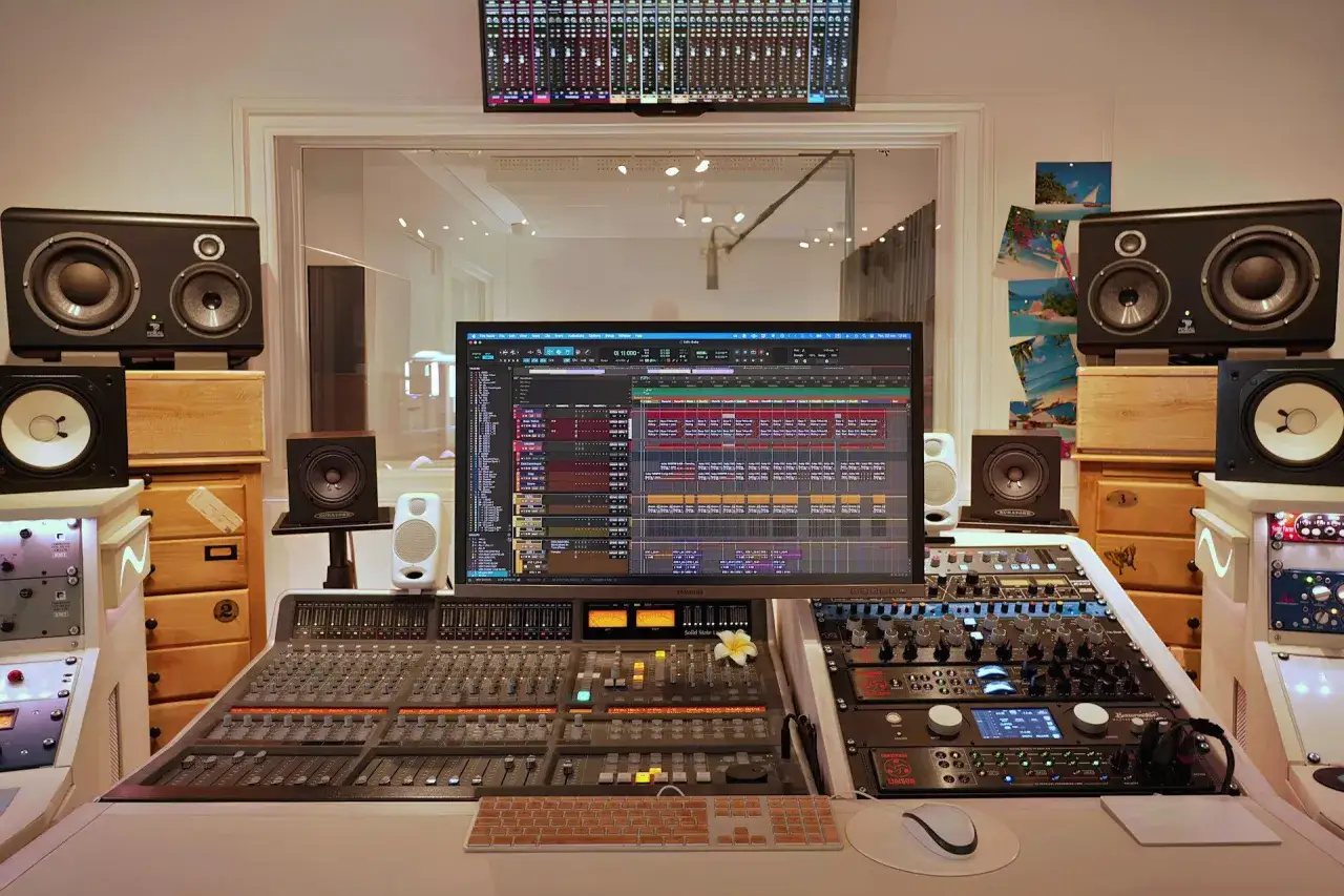 Un studio de production musicale avec une console de mixage, des moniteurs, un écran d'ordinateur affichant une station de travail audio numérique et des enceintes.