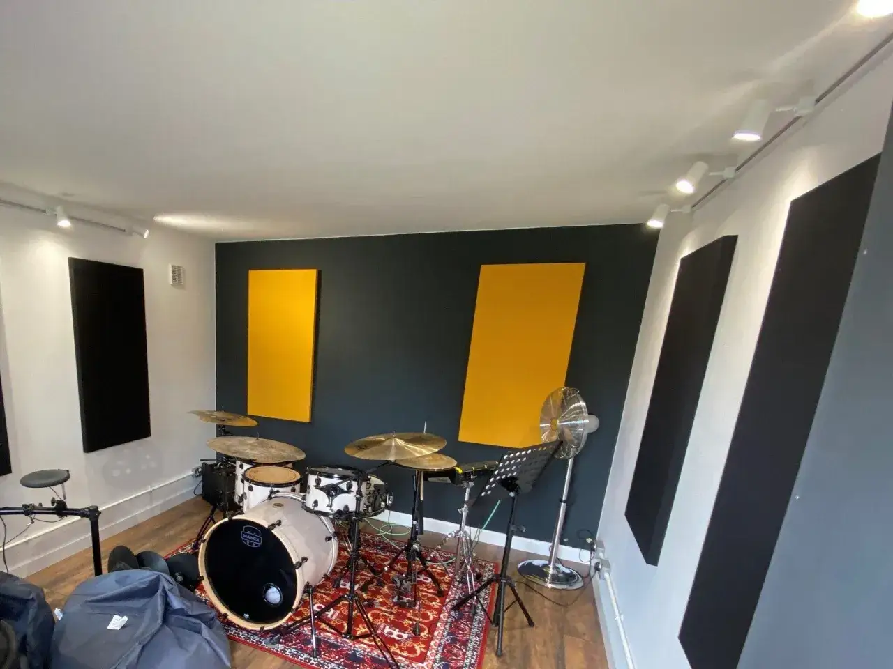 Batterie sur un tapis rouge, avec des panneaux acoustiques jaunes et noirs sur les murs. Le placement batterie est idéal pour l'enregistrement.