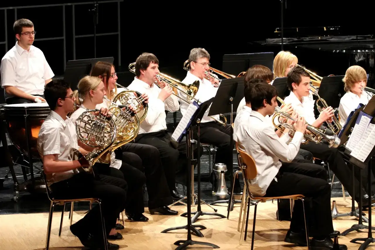 Un orchestre joue, plusieurs musiciens tiennent un gros instrument à vent, comme des cors d'harmonie et des trombones.