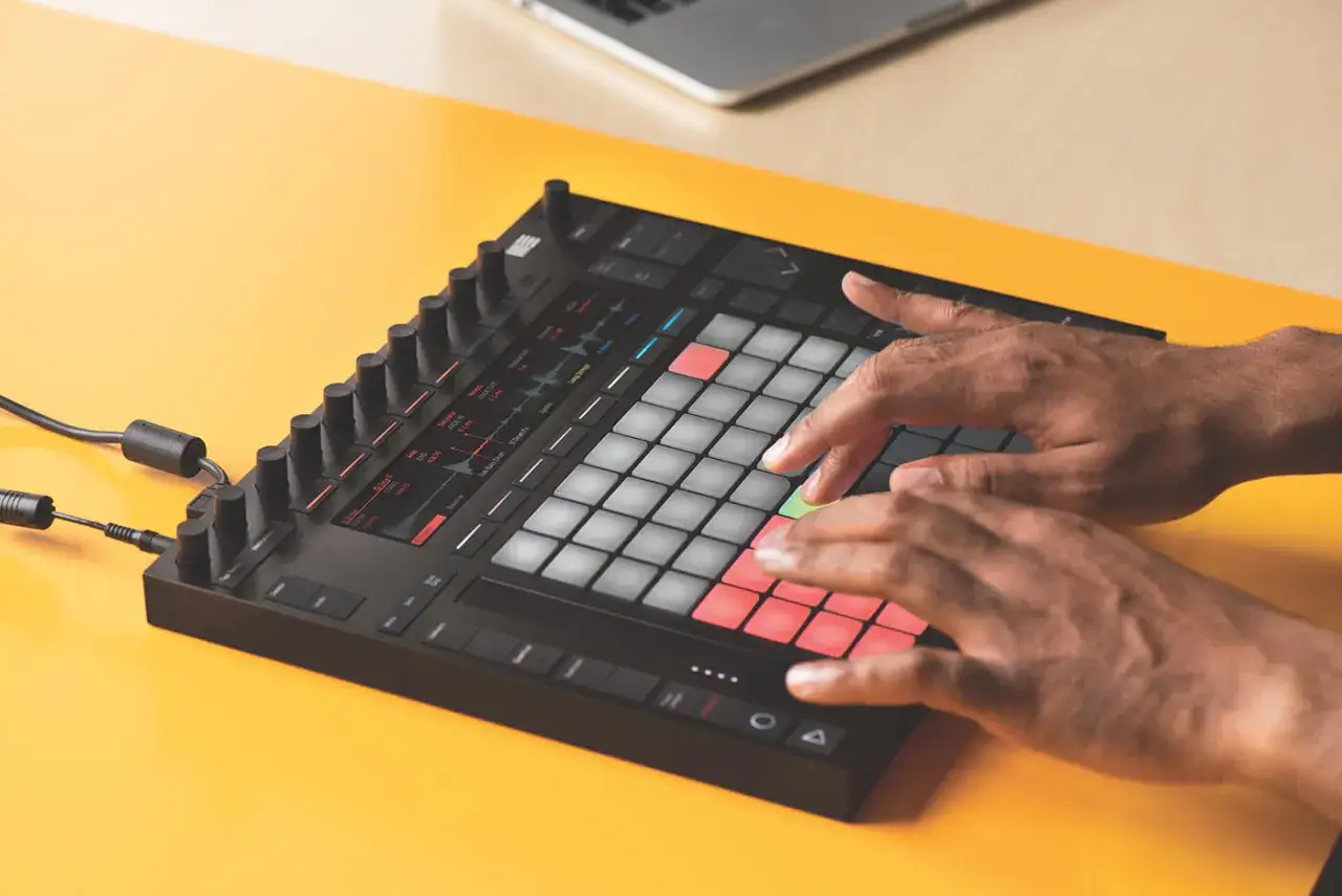 Mains jouant sur un contrôleur pour un tuto Ableton Live 11. Les pads lumineux créent une ambiance créative.