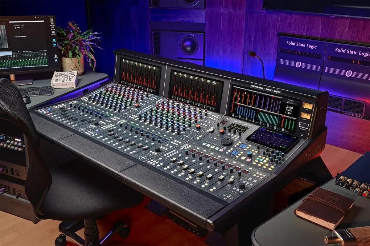 Console studio d'enregistrement professionnel avec de nombreux faders, boutons et écrans lumineux.