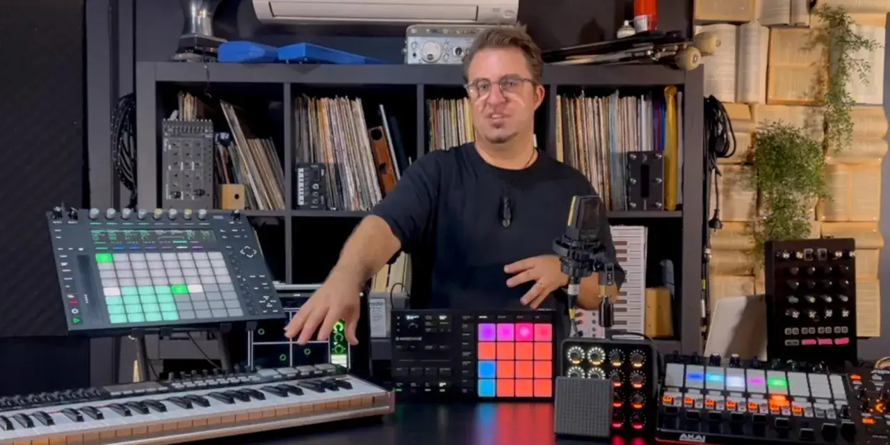 Un homme présente plusieurs instruments midi, dont un clavier, des pads lumineux et des contrôleurs, dans un studio de musique.