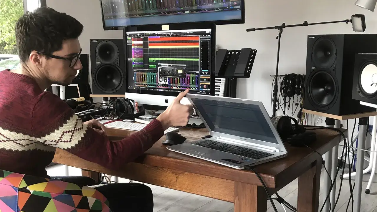 Un jeune homme apprend le mixage audio dans son studio. Il manipule une table de mixage sur son ordinateur.