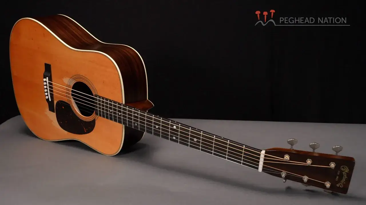 Une guitare acoustique Martin D-28, avec son corps en bois clair et sombre, posée sur un fond gris.