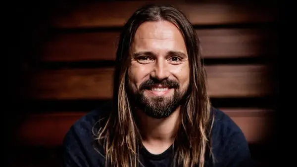 Un homme souriant aux longs cheveux bruns et à la barbe, peut-être un des compagnons d'écriture de Max Martin.